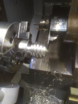Une pièce en aluminium en forme de bout de cuillère à miel. Cette pièce est dans une machine industrielle qui est un tour à 3 axes permettant son travail de manière sécurisée